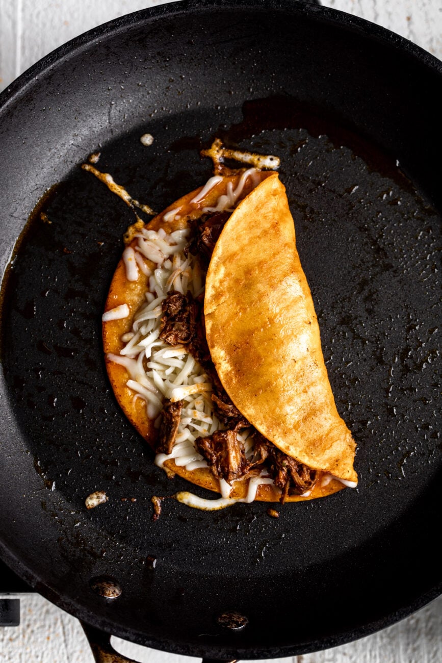 quesobirria taco with melted cheese in pan.