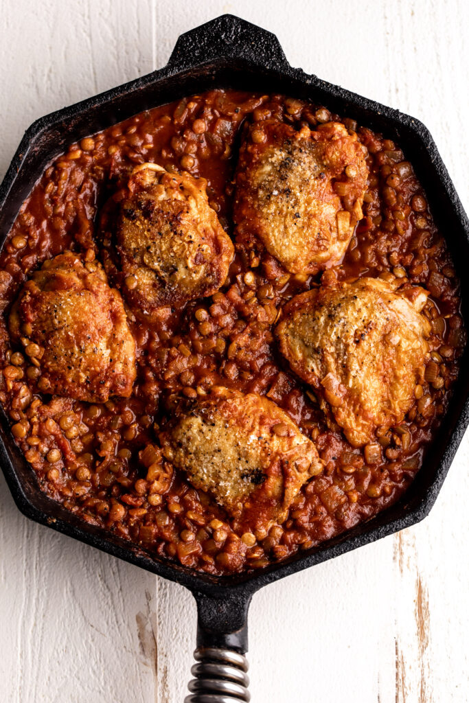 One-Pan seared Chicken Thighs with Harissa Lentils and tomatoes in cast iron pan