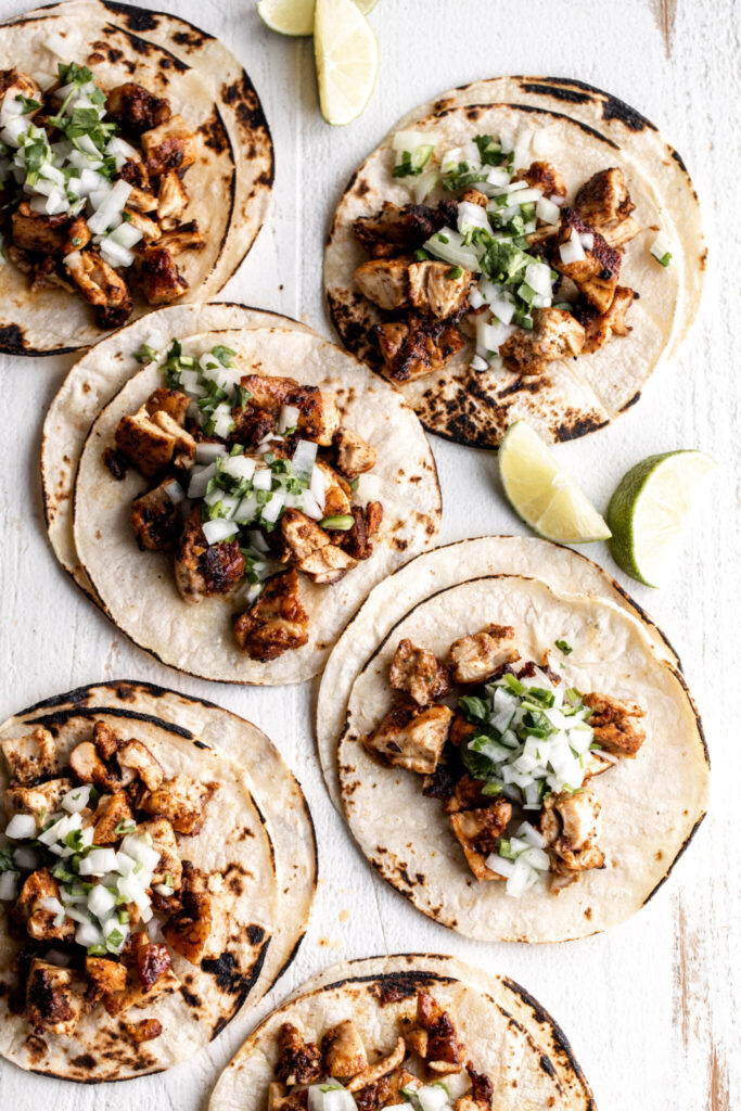 Mexican chicken street tacos topped with diced onion and cilantro and lime wedges best chicken recipes