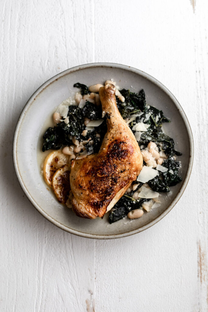 whole roast chicken legs with white beans and kale in stone dish