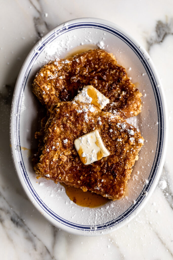 cornflake french toast with butter and maple syrup on oval platter.