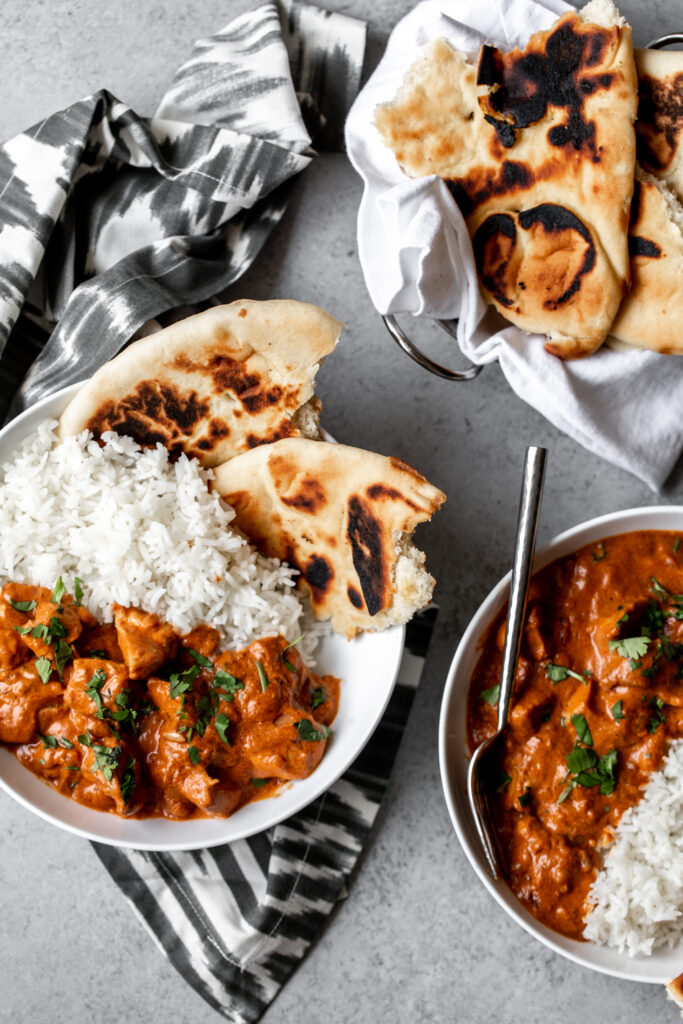 Butter Chicken (Murgh Makhani) in serving bowls over rice with side of naan bread