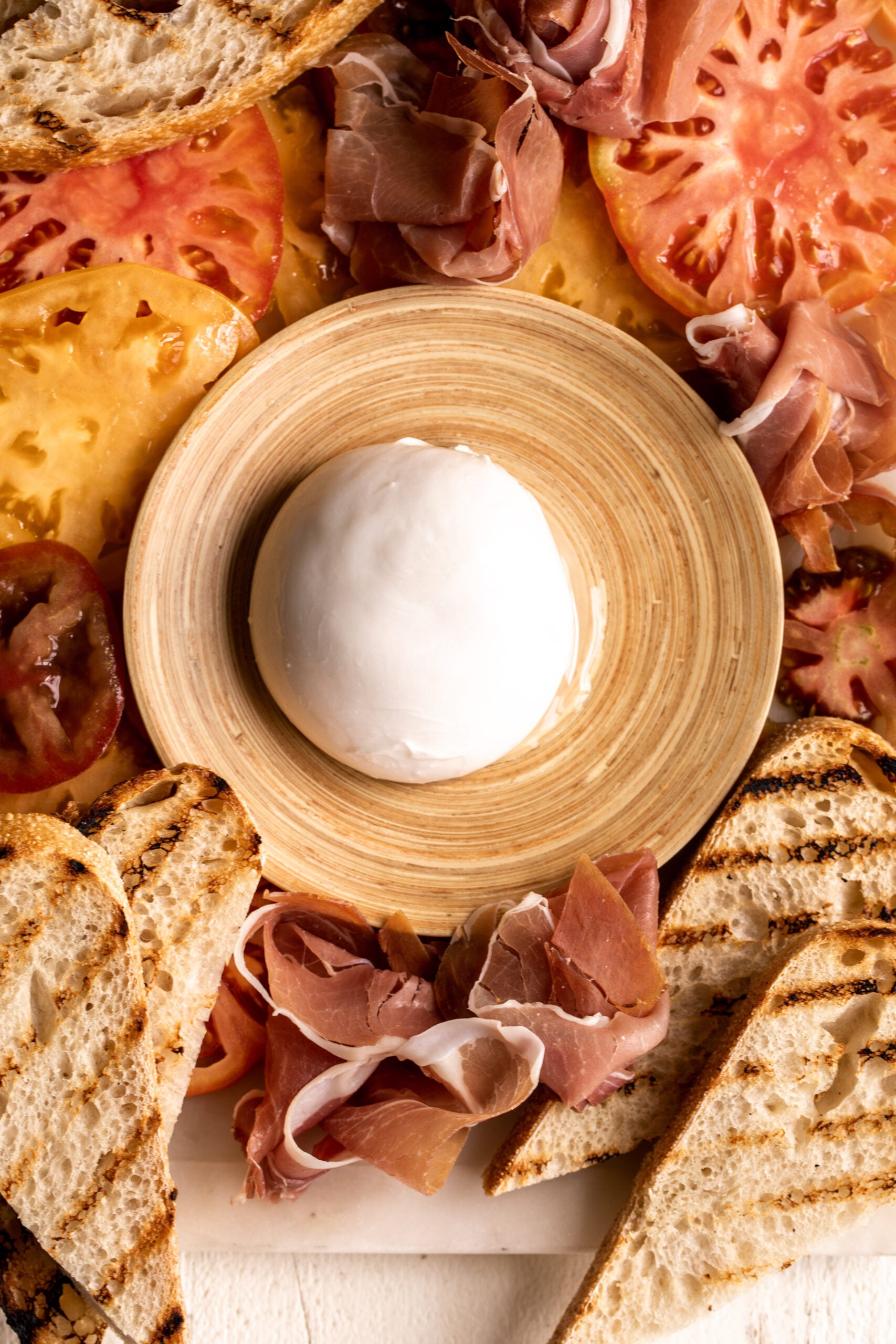 burrata on dish with prosciutto and grilled bread.