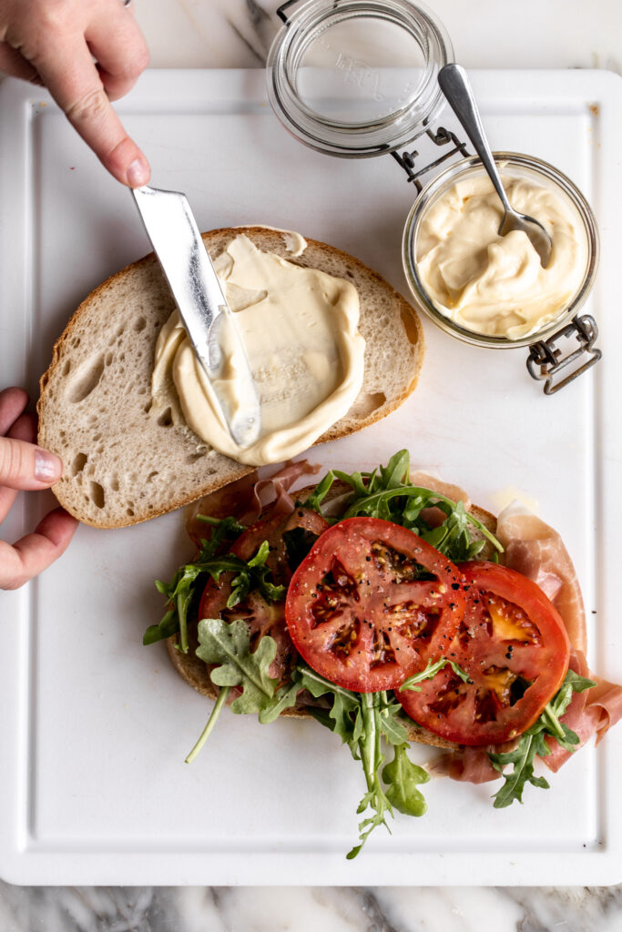 person using homemade mayonnaise in making a sandwich