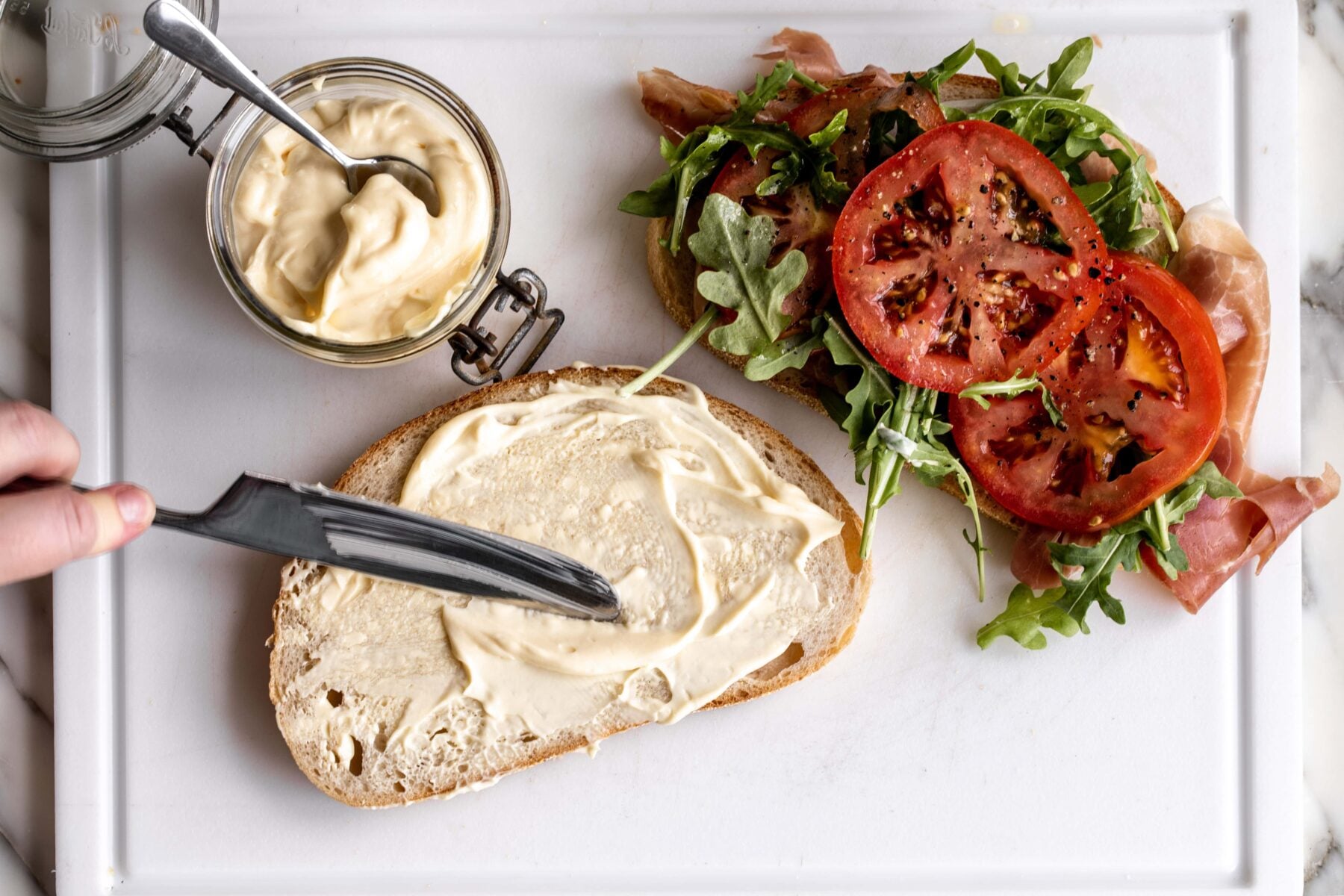 homemade mayonnaise spread over slice of sourdough bread for BLT sandwich.