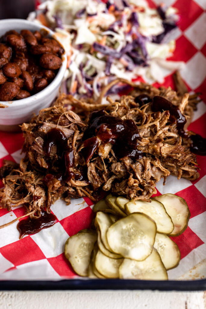 oven braised pulled pork on baking sheet with pickles and coleslaw