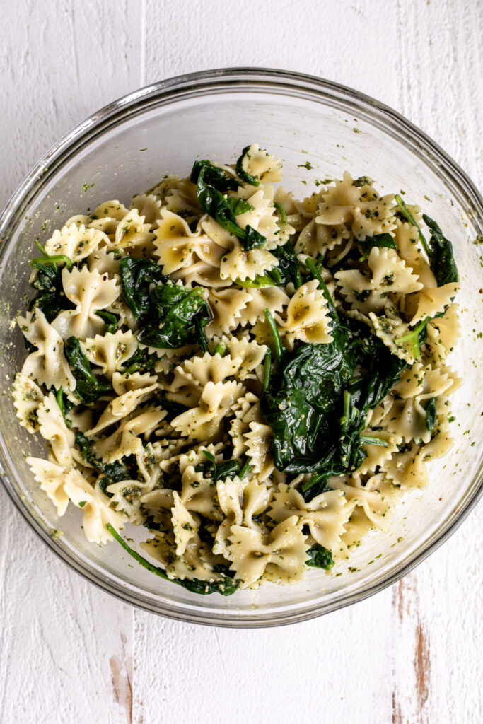 adding oil to pasta and spinach for Pesto Pasta Salad Recipe 