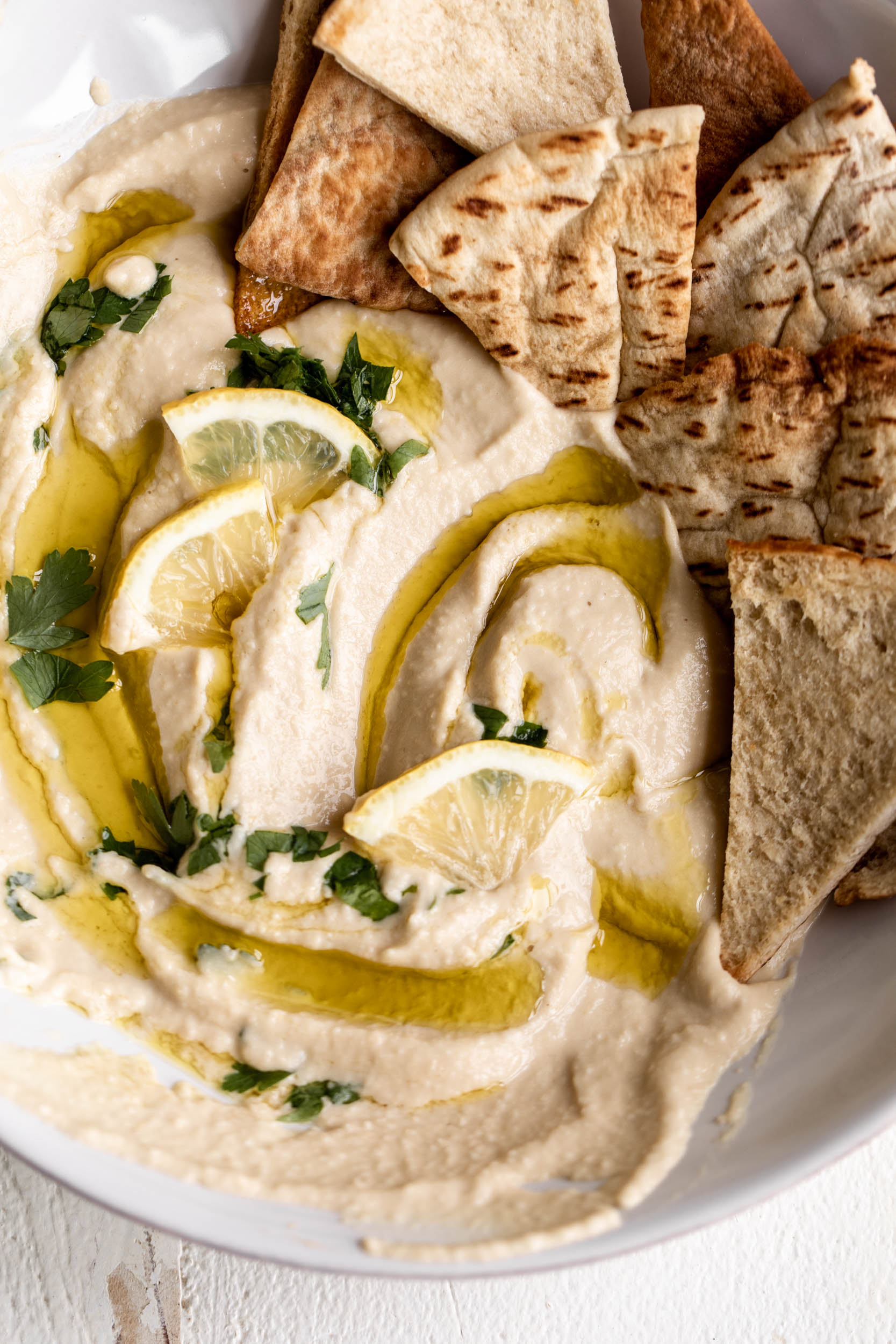 lemon garlic hummus in bowl with olive oil and lemon and pita chips.