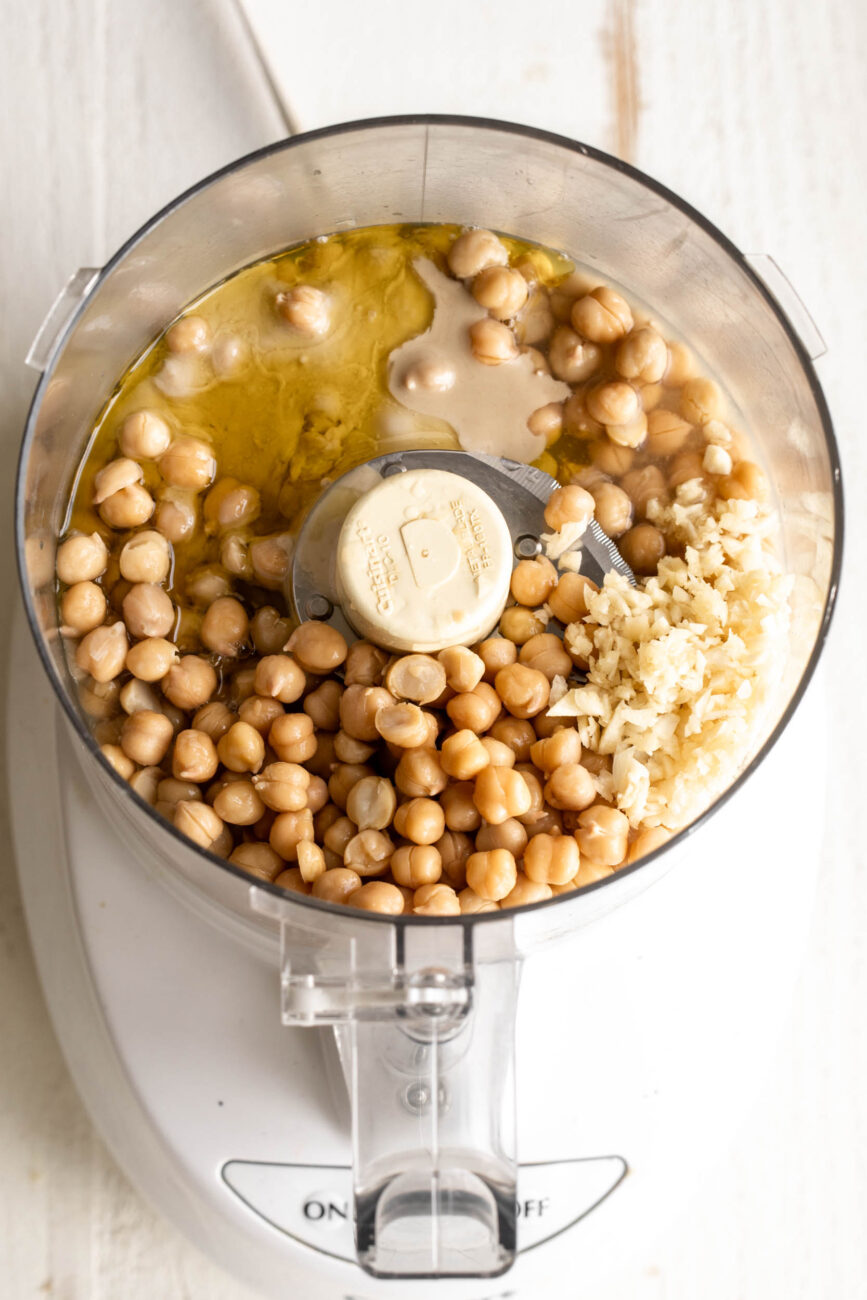 hummus ingredients in food processor with chickpeas, garlic , and tahini.