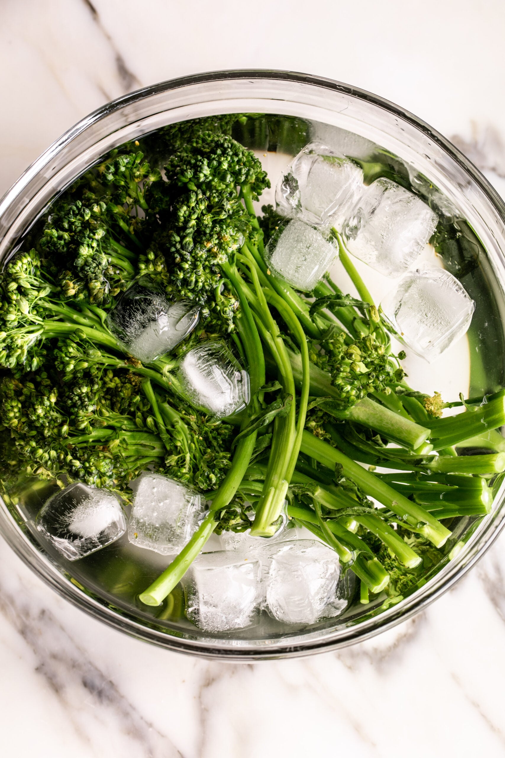 blanched broccolini in bowl of ice water.