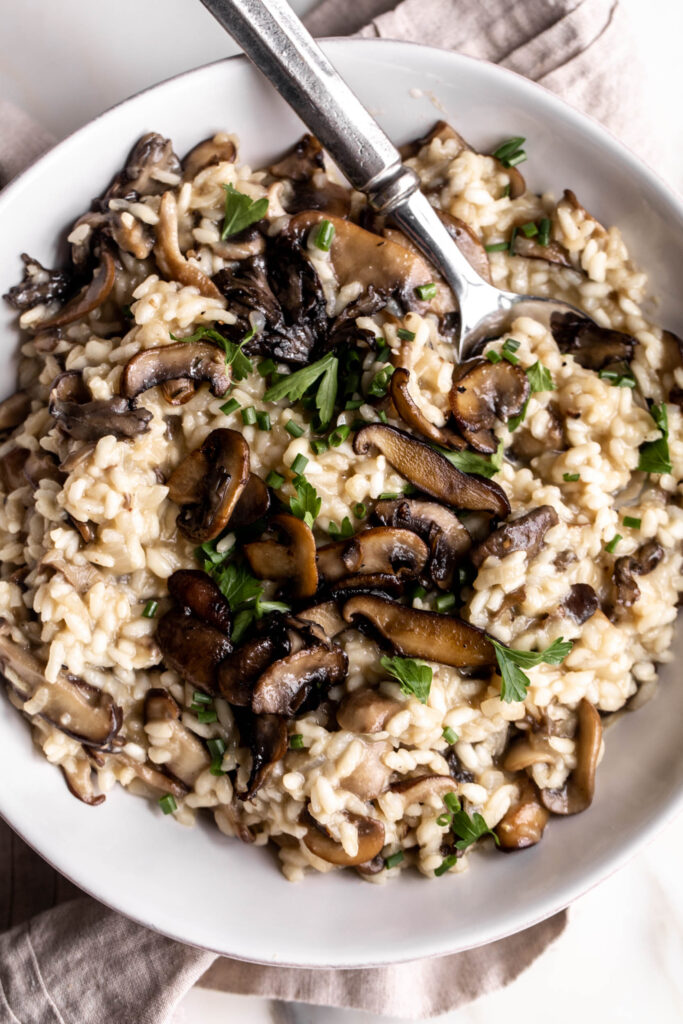 mixed mushroom risotto garnished with parsley and chives in bowl with spoon