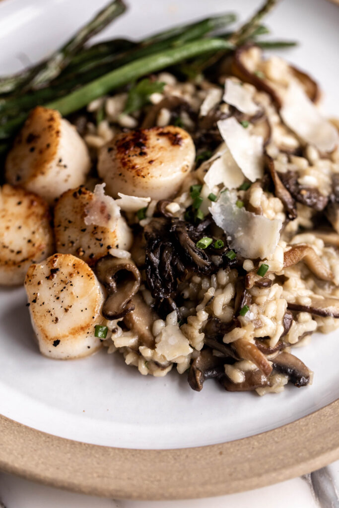 mixed mushroom risotto garnished with parsley and chives with scallops and sautéed green beans