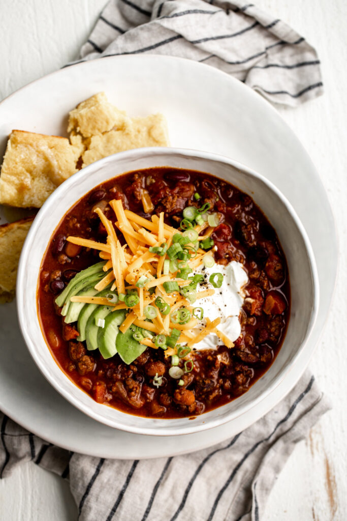 beef chili in a bowl with sour cream cheese avocado and green onion with fritos chips
