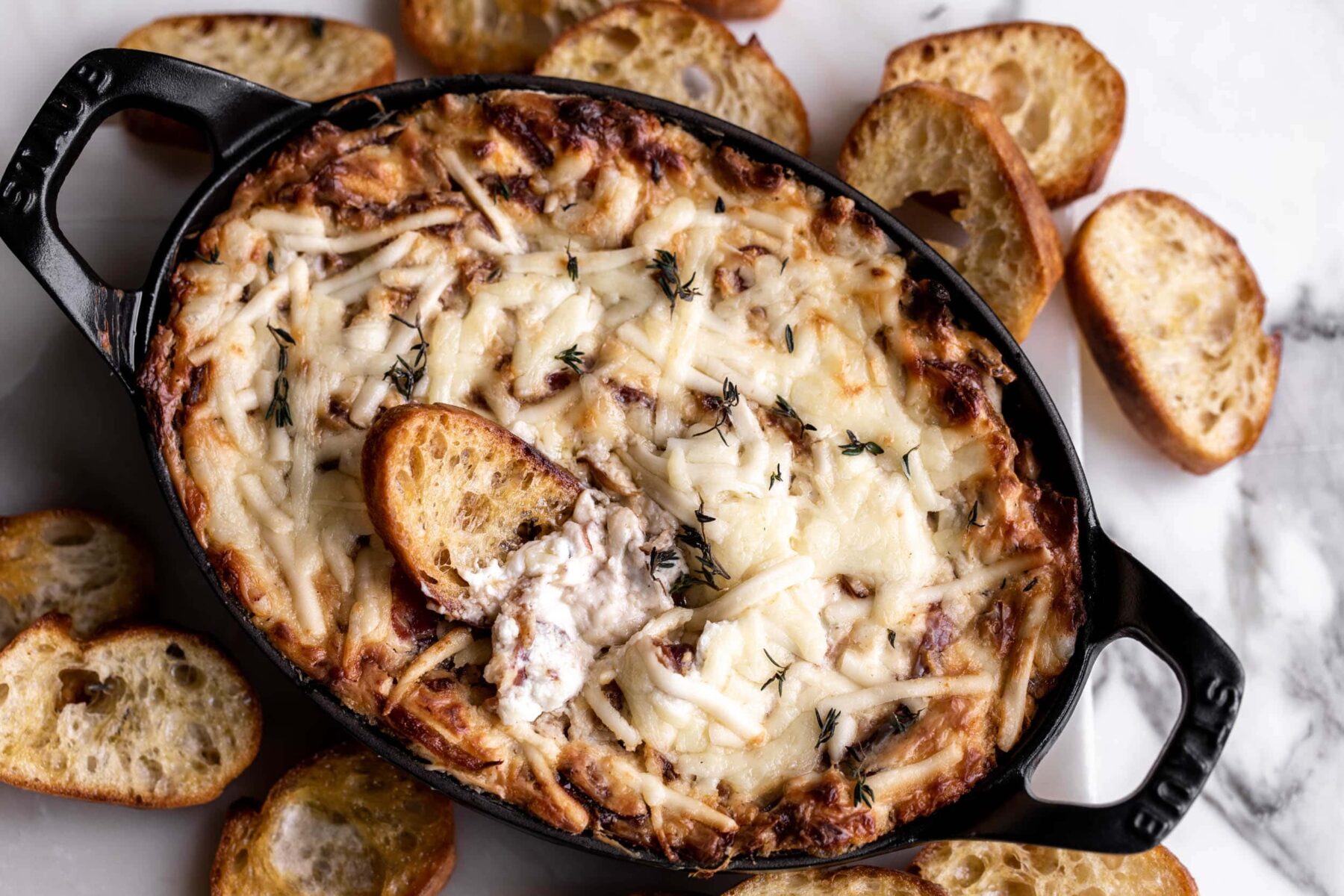 Baked Cheesy Onion and Bacon Dip in small cast iron dish with crostini.