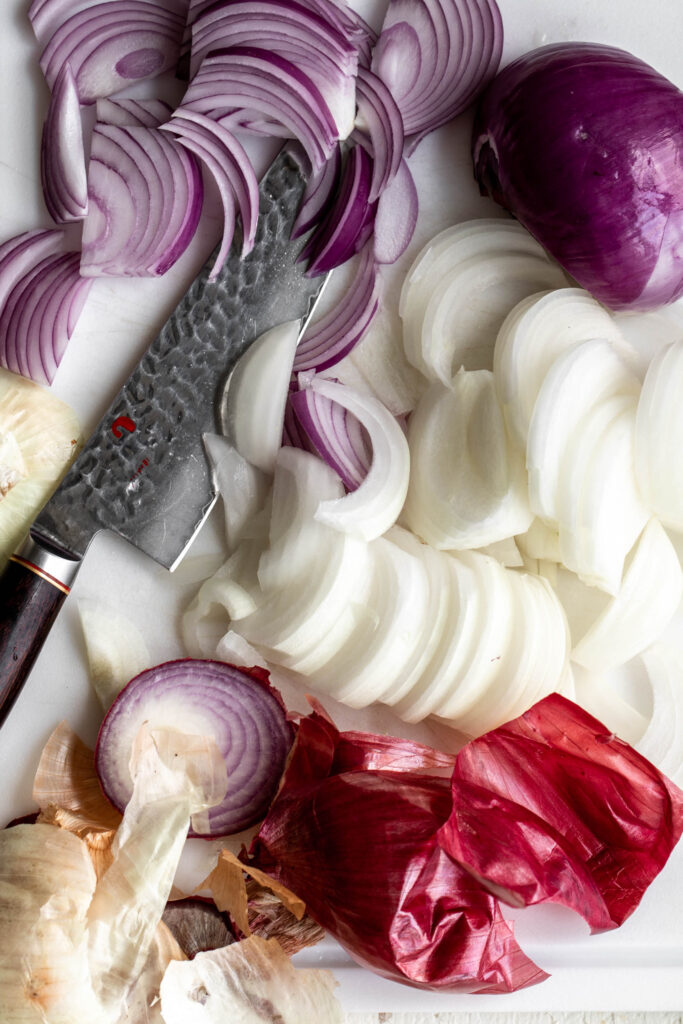 thinly sliced yellow and red onions on white cutting board with chef knife for bacon dip