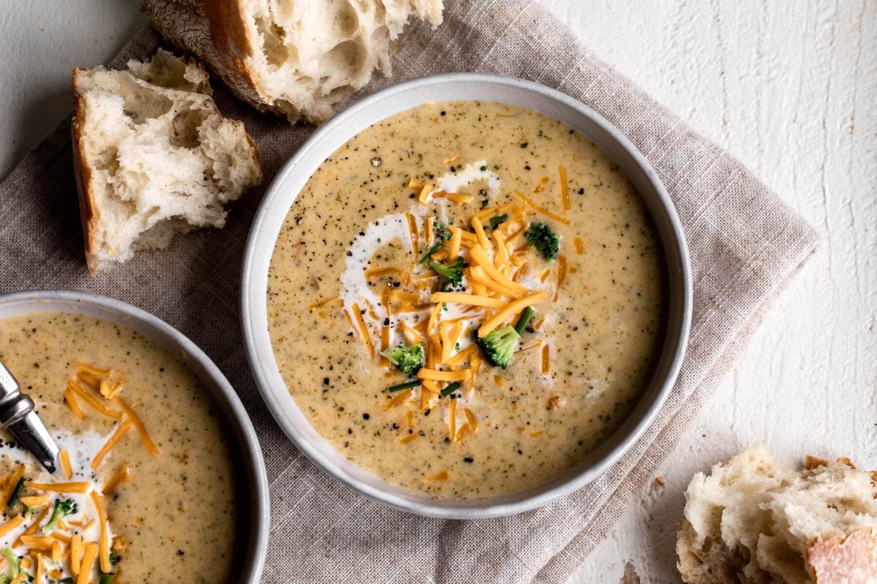 broccoli cheddar soup in bowls topped with cheddar cheese and chives with bread.