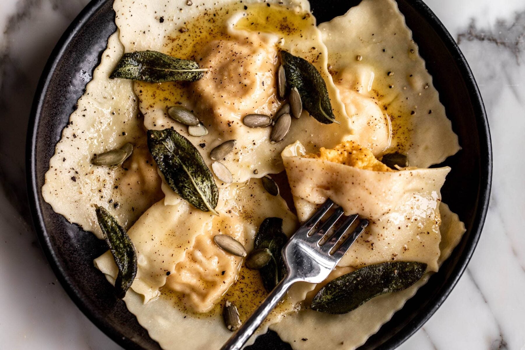 homemade butternut squash and ricotta ravioli with brown butter sage and pepitas in black bowl.