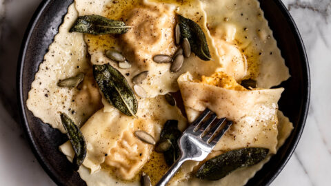 homemade butternut squash and ricotta ravioli with brown butter sage and pepitas in black bowl
