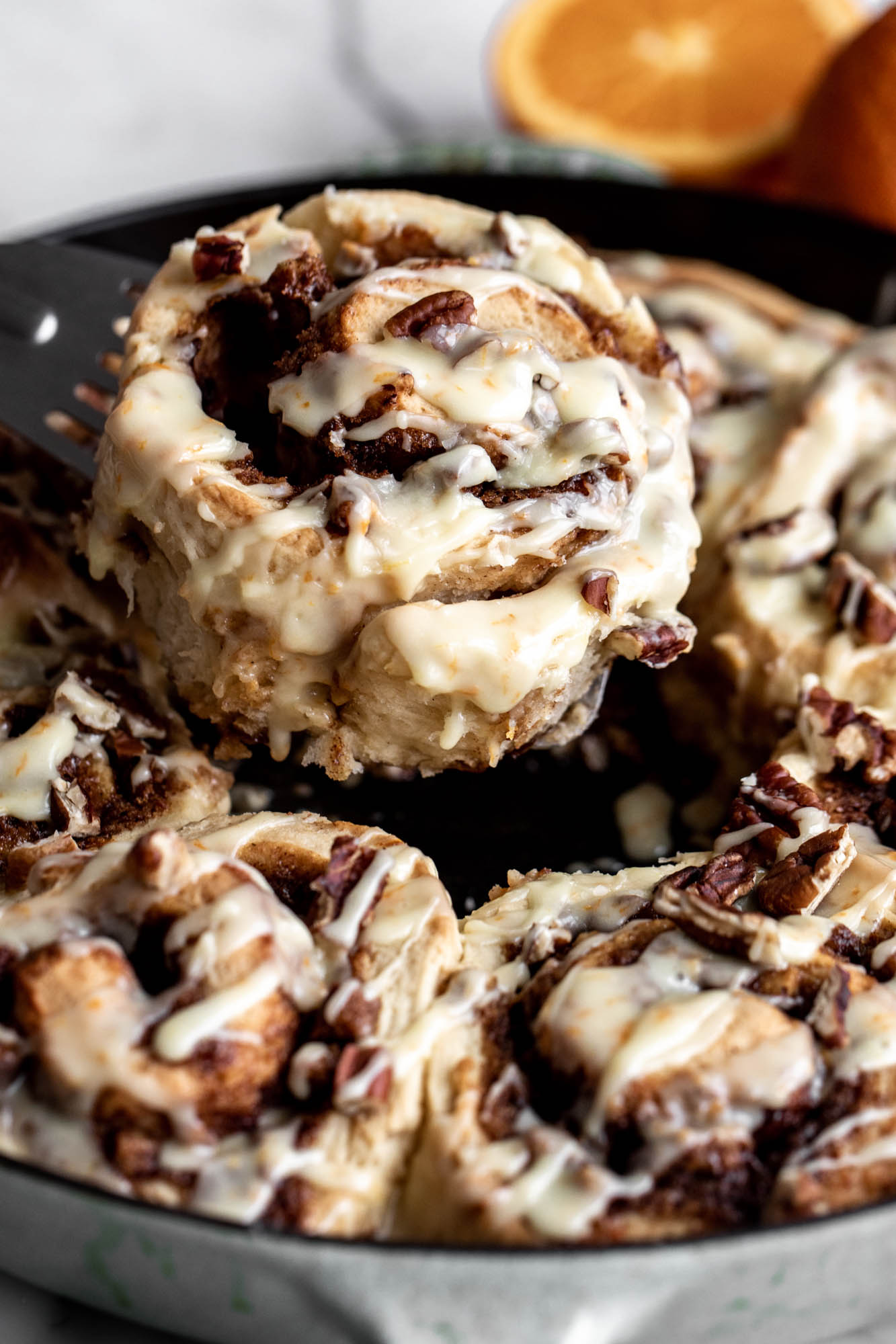 individual orange roll with chopped pecans lifted from pan.