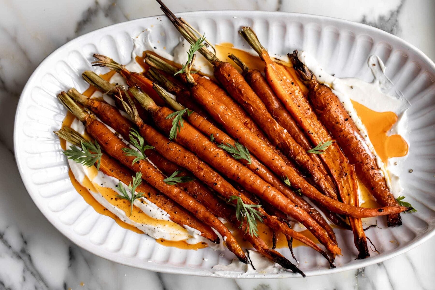 roasted carrots with whipped ricotta and chili butter on white serving platter holiday vegetable side.