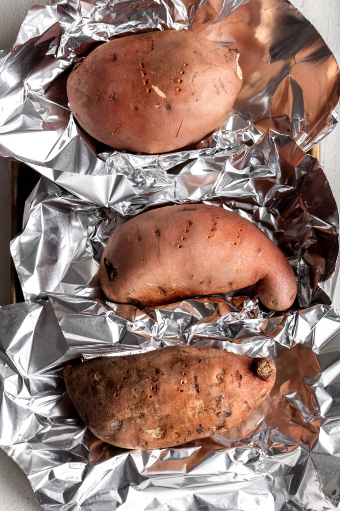 sweet potatoes in aluminum foil on baking sheet