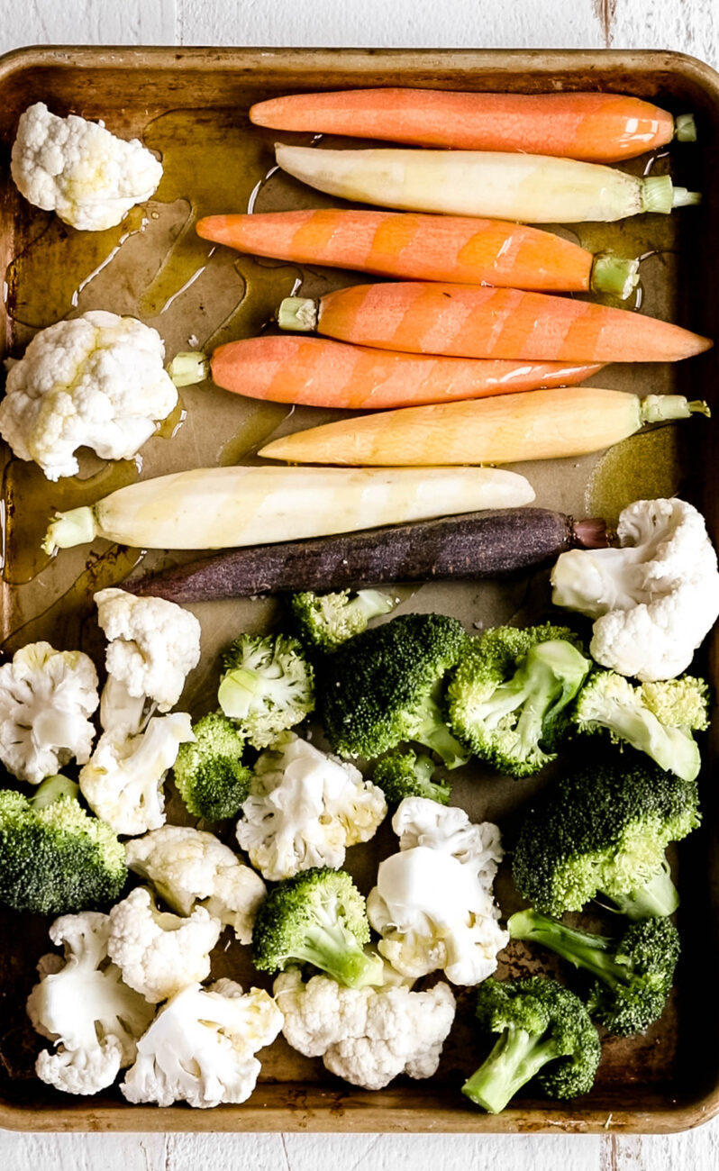 carrots broccoli and cauliflower in olive oil on baking sheet.
