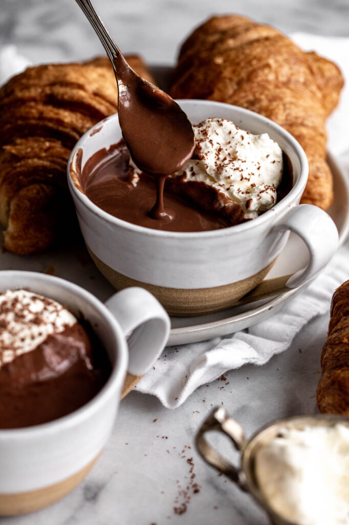 French hot chocolate thick and creamy on spoon with side of croissants.