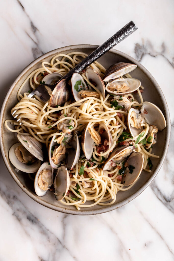 spaghetti alle vongole in stone bowl with fork garnished with parsley.
