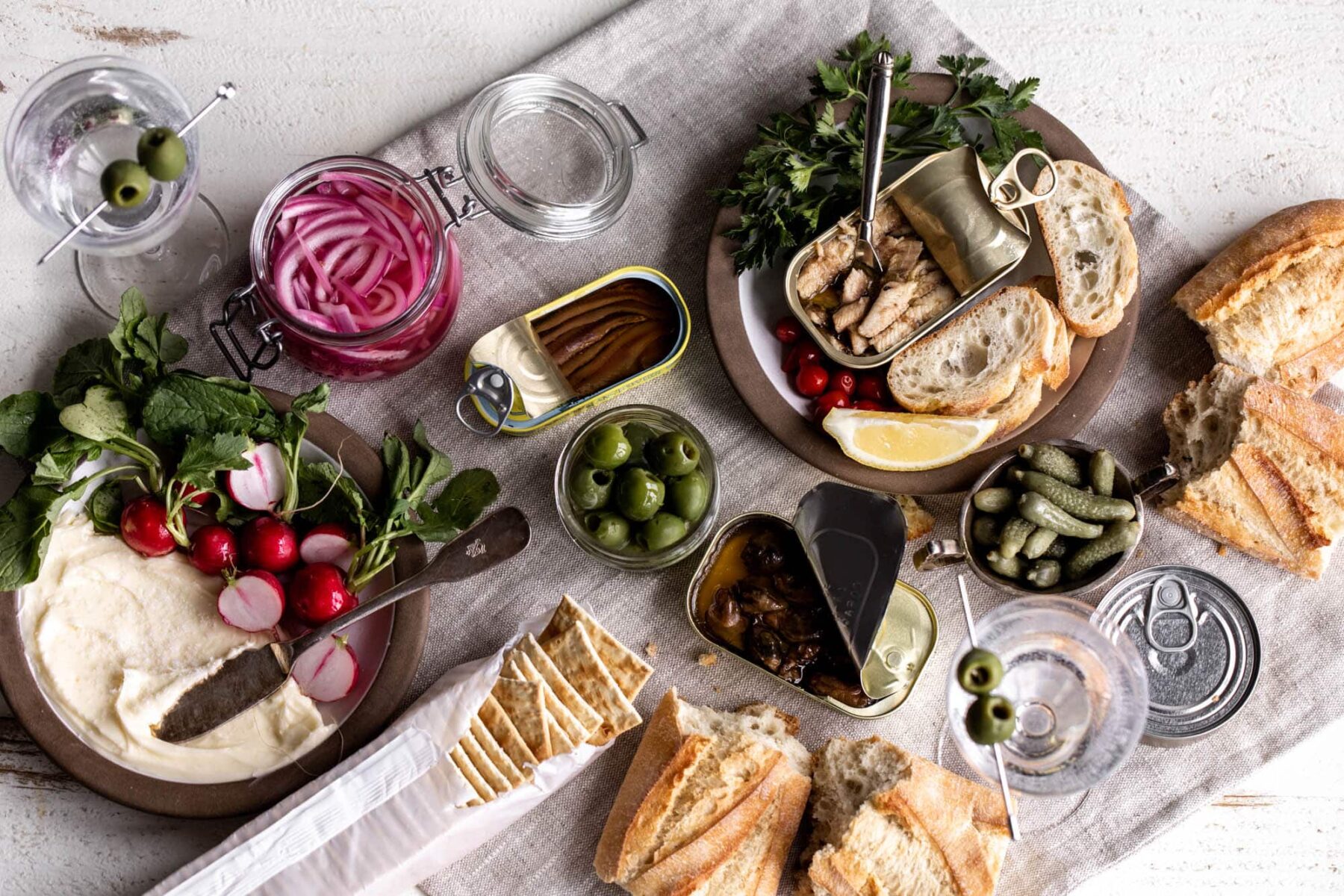 tinned fish spread with crackers, bread, pickles and radish.