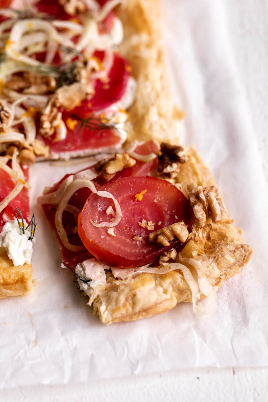 single slice of roasted beet and goat cheese tart with fennel slaw and pistachio on puff pastry.