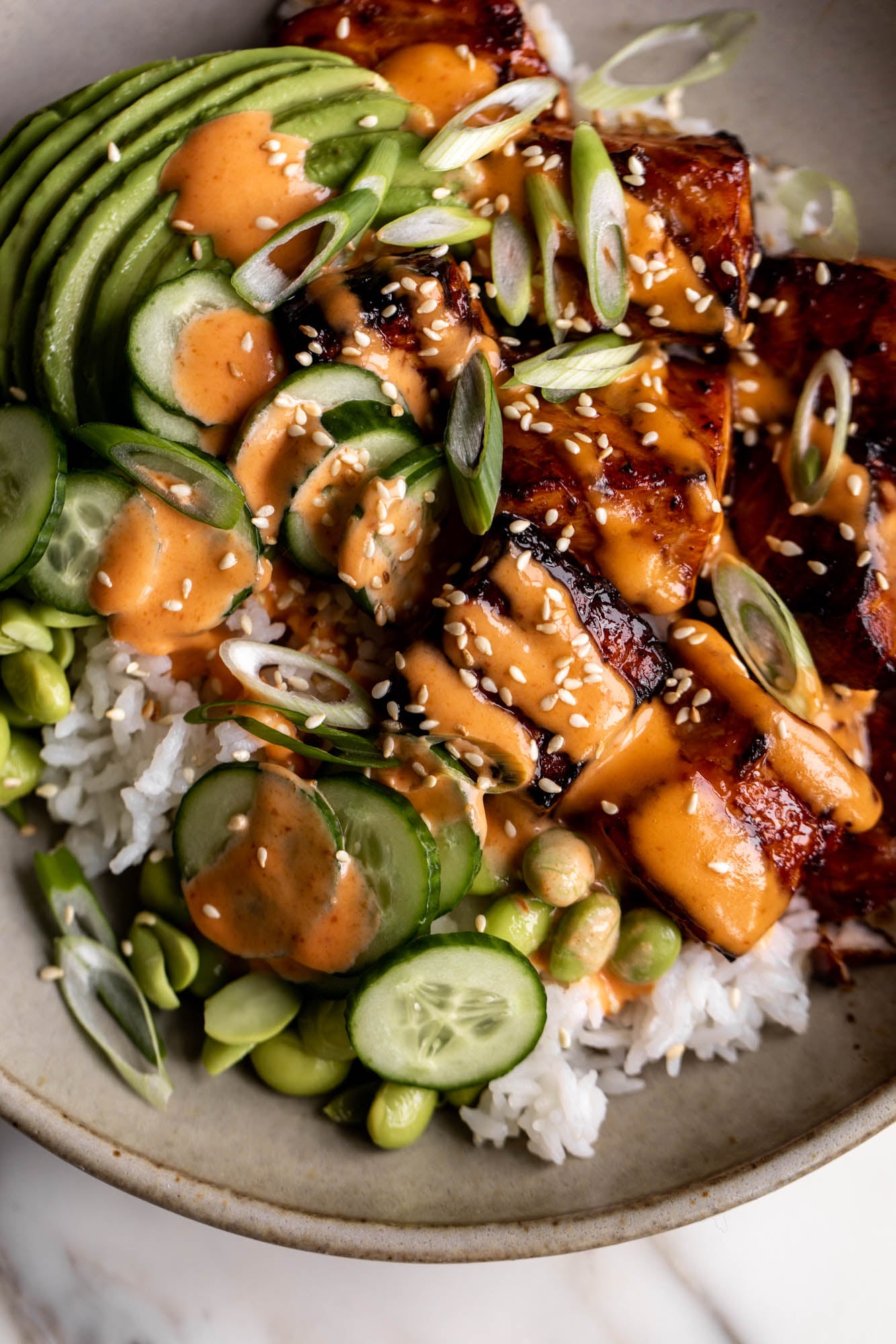 teriyaki salmon bowls with sriracha mayonnaise with sliced cucumber and edamame.