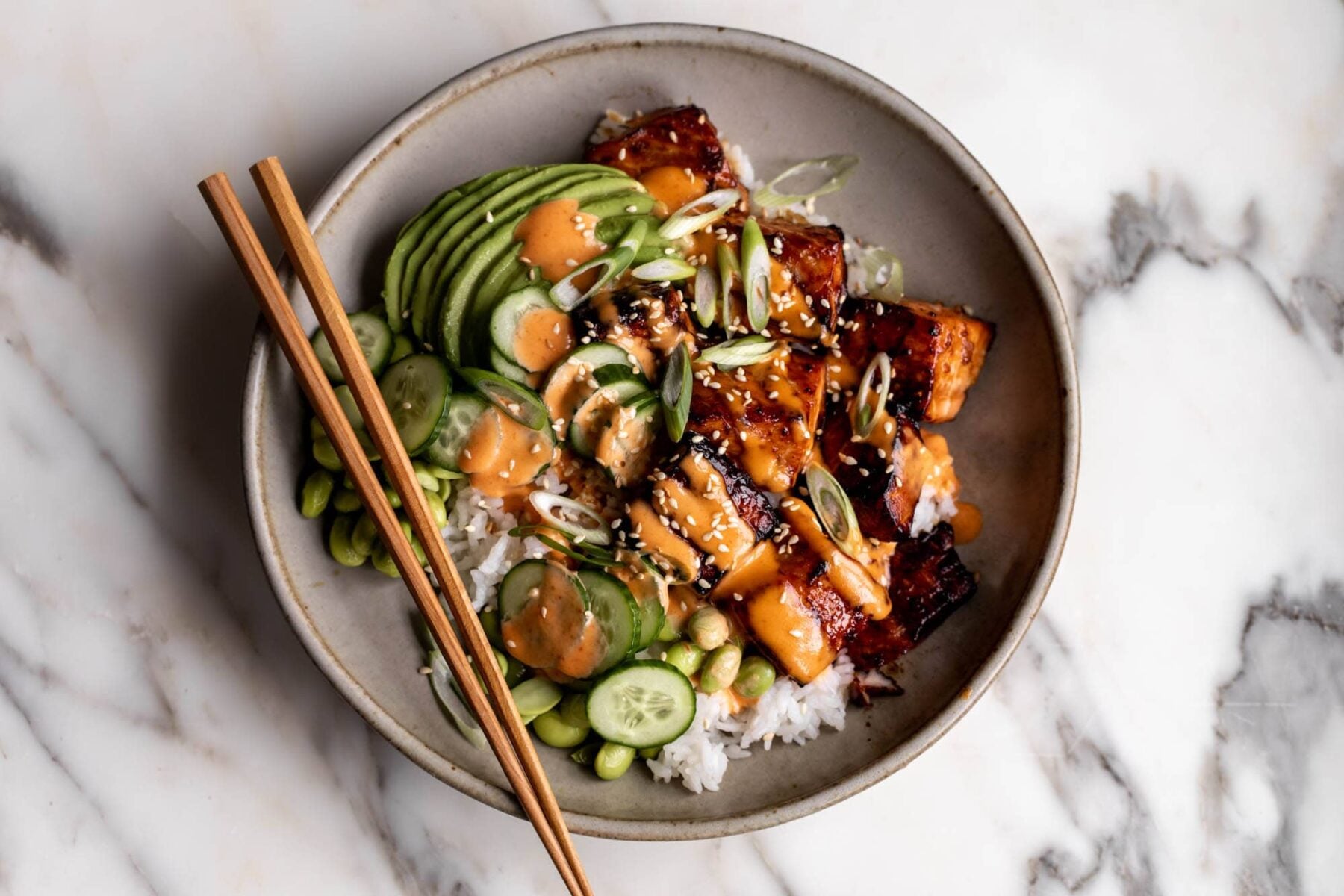 teriyaki salmon rice bowls with sliced cucumber and edamame.