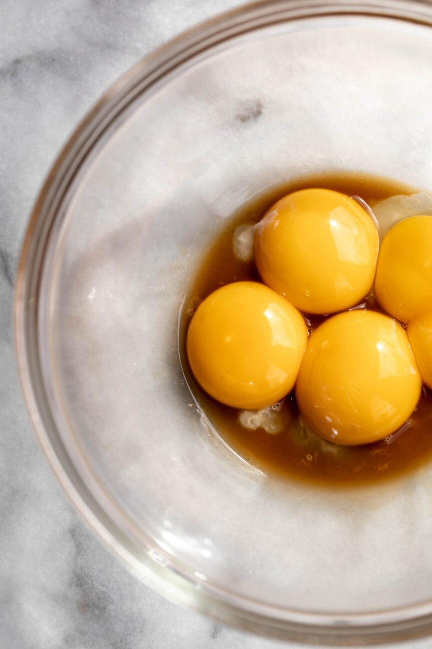 Egg yolks in bowl with brown liquid.