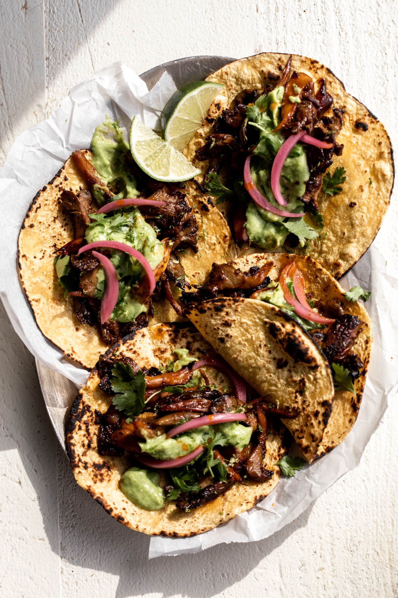 Crispy adobo mushroom tacos with avocado-tomatillo salsa and pickled onions on corn tortillas.