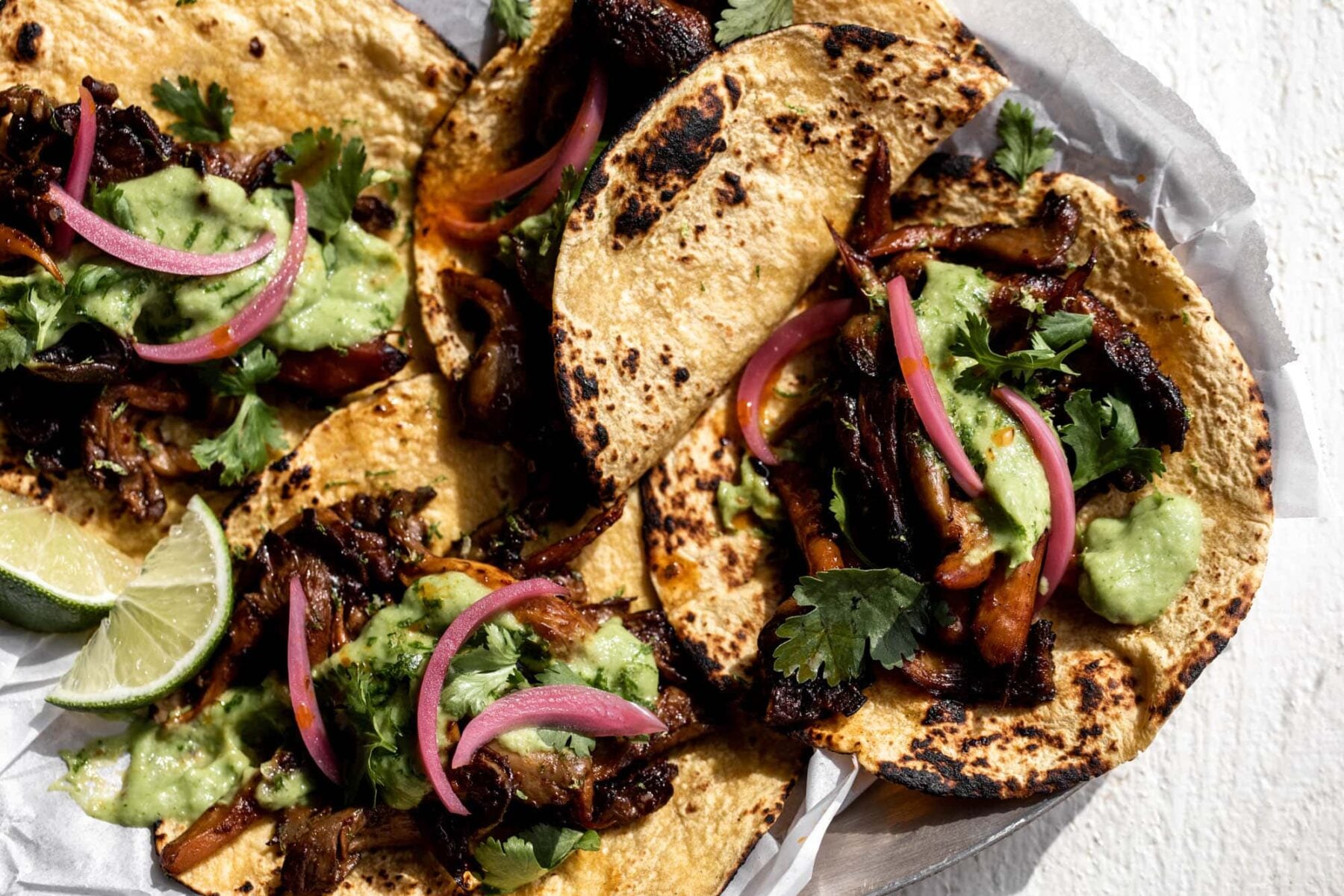 Crispy adobo mushroom tacos with avocado-tomatillo salsa and pickled onions on corn tortillas.