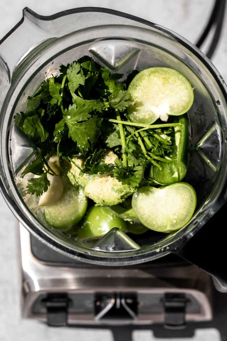 Tomatillo-Avocado Salsa Verde ingredients piled in blender closeup in harsh sunlight.