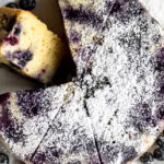 Lemon blueberry cake garnished with powdered sugar cut into slices.