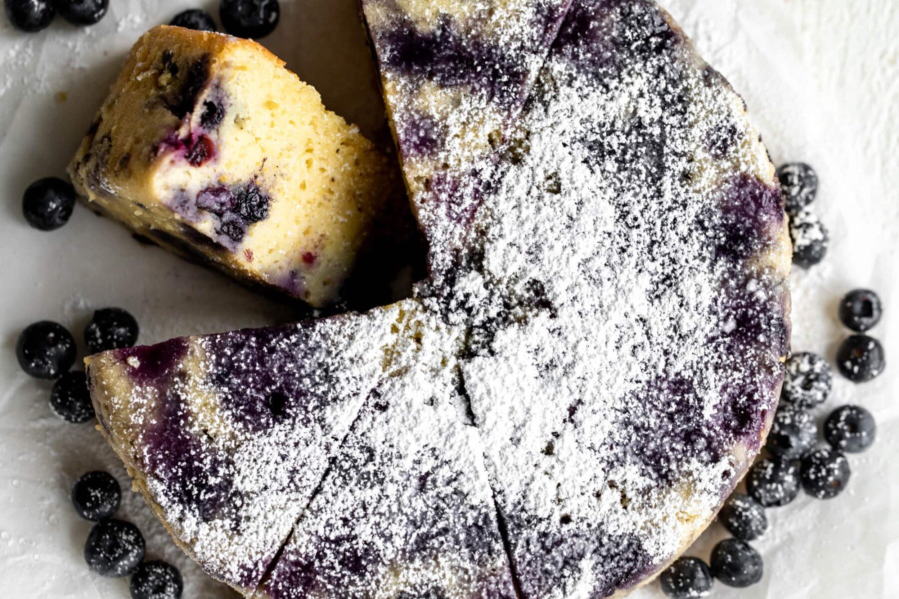 Lemon blueberry cake garnished with powdered sugar cut into slices.