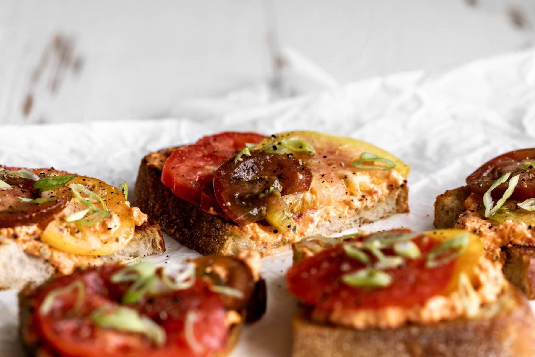 pimento cheese toasts topped with heirloom tomatoes and green onions.