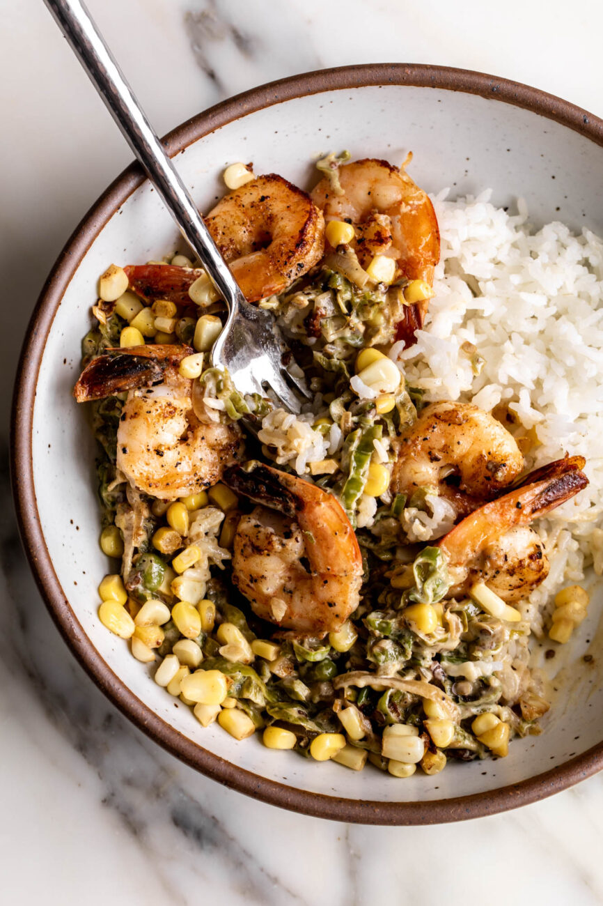 fork full of sautéed shrimp with creamed shishito peppers and corn.
