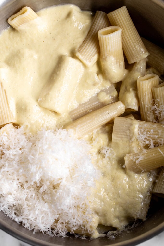 creamy corn pasta sauce with cooked rigatoni noodles and parmesan cheese in pot