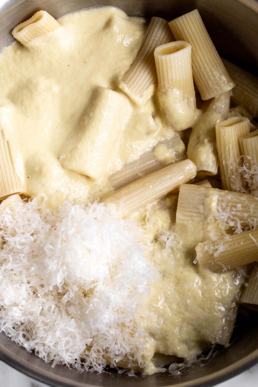 creamy corn pasta sauce with cooked rigatoni noodles and parmesan cheese in pot.