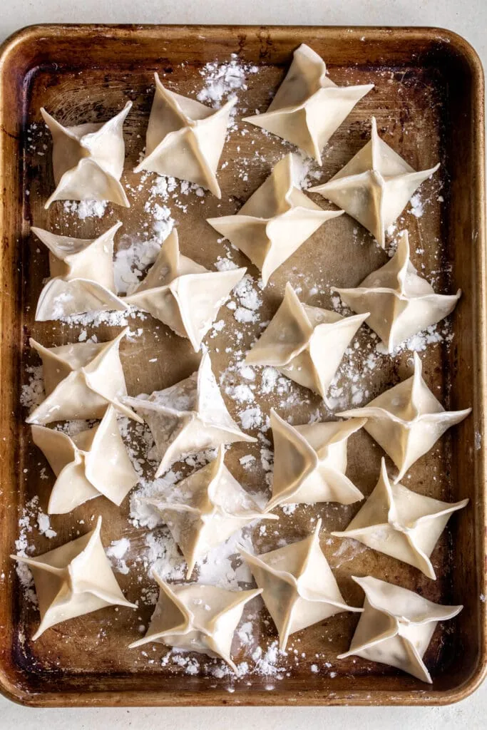 assembled and folded crab rangoons on baking sheet dusted with cornstarch.