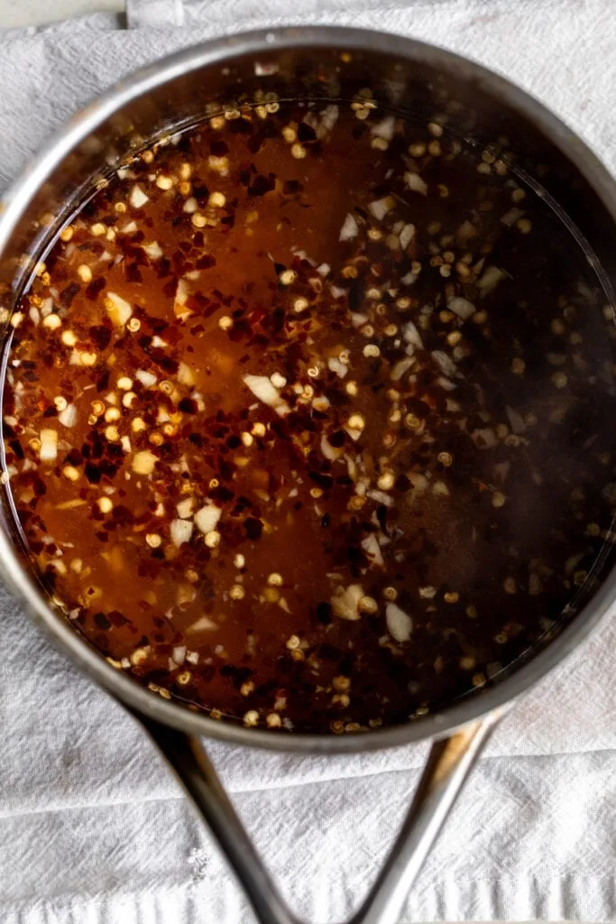 homemade orange sweet chili sauce simmered in pot with chili flakes and garlic. 