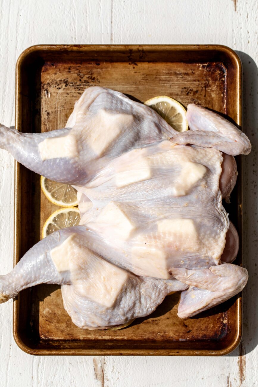 spatchcocked lemon and garlic roast chicken with butter under the skin and lemon slices.