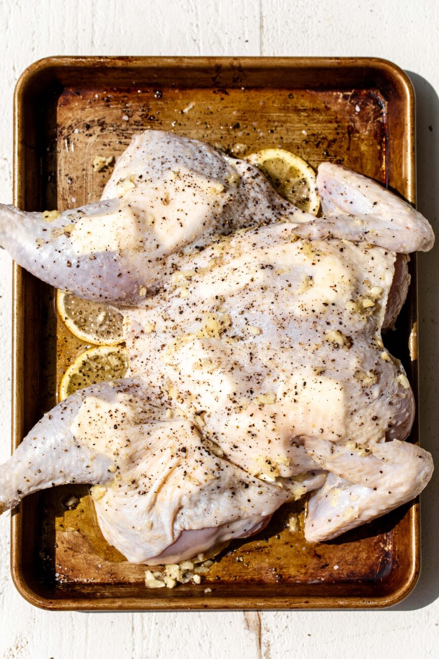 spatchcocked lemon and garlic roast chicken with butter under the skin and lemon slices seasoned with salt and pepper.
