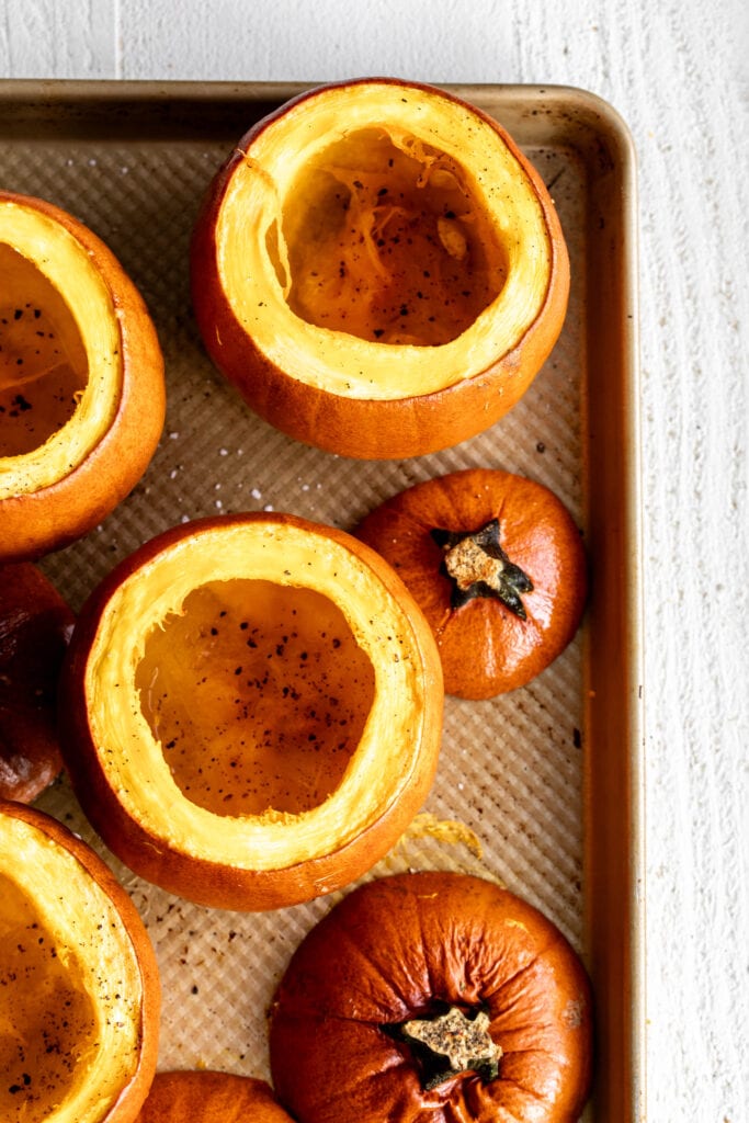 roasted sugar pumpkins with tops cut off and scooped out on baking sheet.