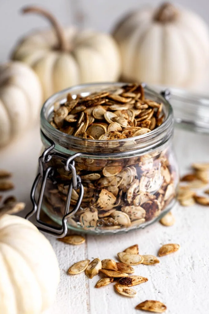 roasted ranch pumpkin seeds in a glass jar with small mini white pumpkins