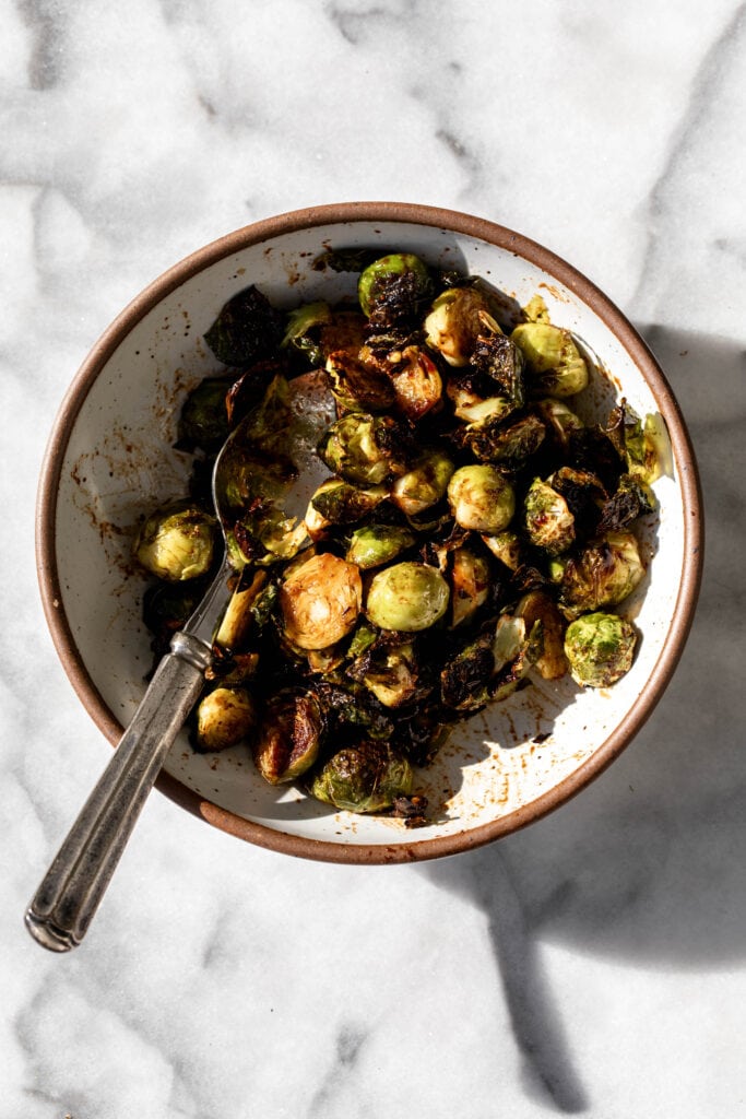 balsamic sriracha roasted brussels sprouts halved in serving bowl with spoon on marble table