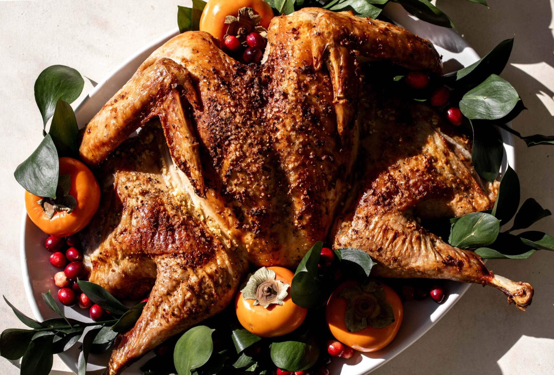 garlic butter spatchcock thanksgiving turkey on platter with persimmons and greens.